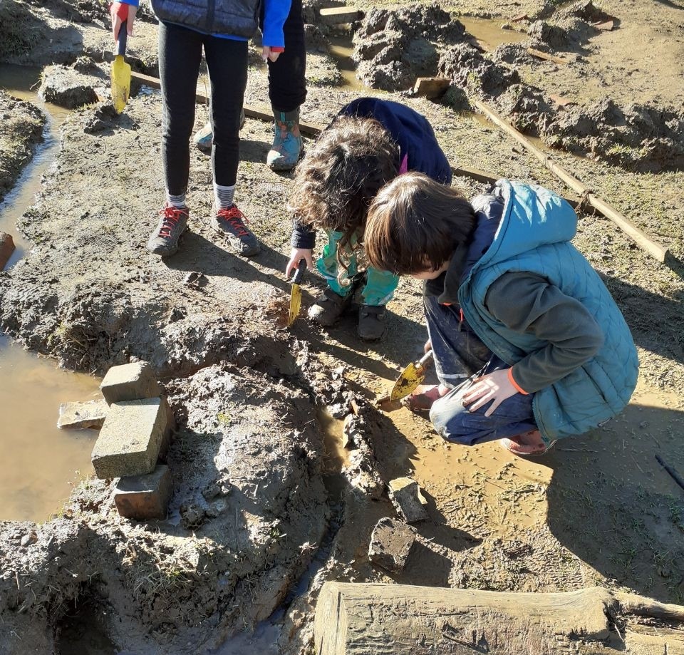 Children playing in mud and water creating a series of structure with trowels through which water flows.