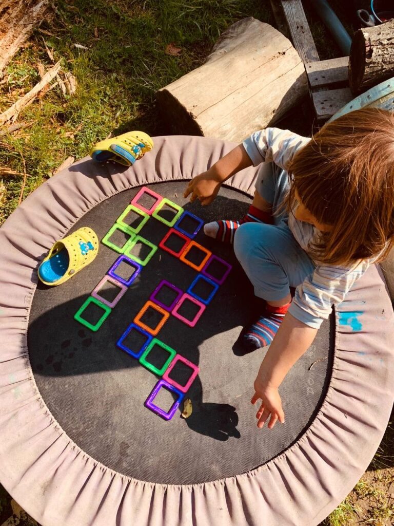 A child plays on a trampoline with a series of brightly coloured squares arranging them in a pattern.