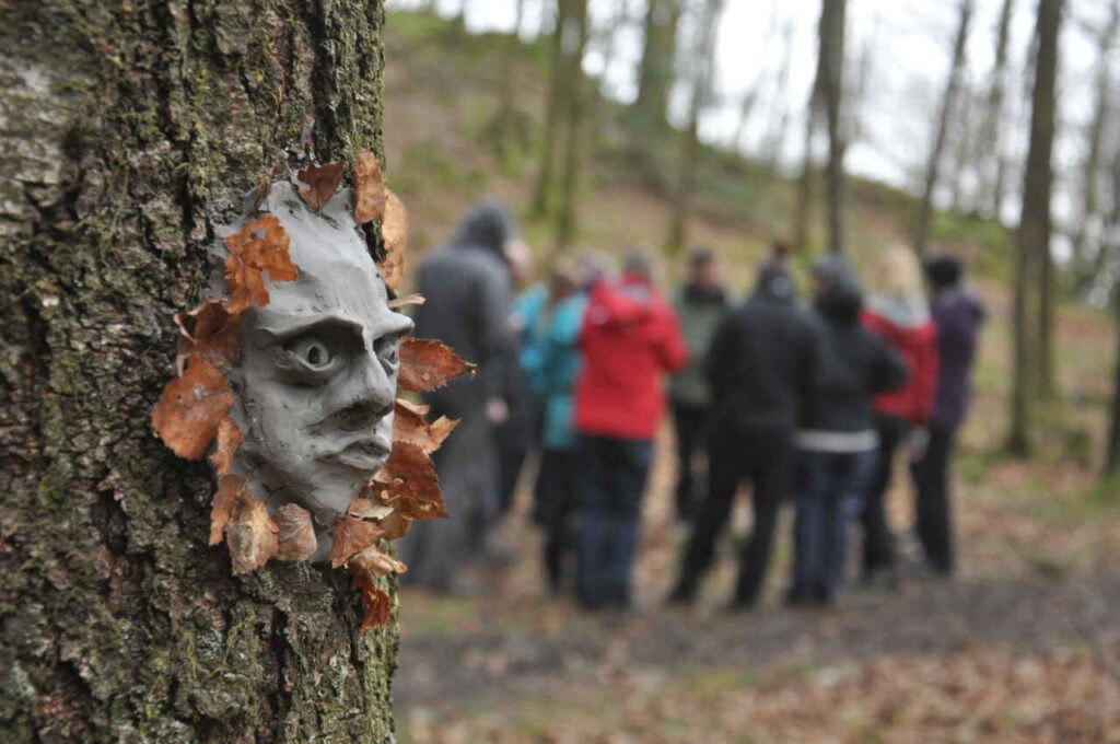 A group of leaders gather in front f a face made of clay attached to a tree, with leaves as a kind of mane